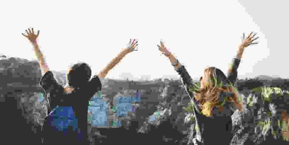 two-hikers-raising-arms-at-cliff-side